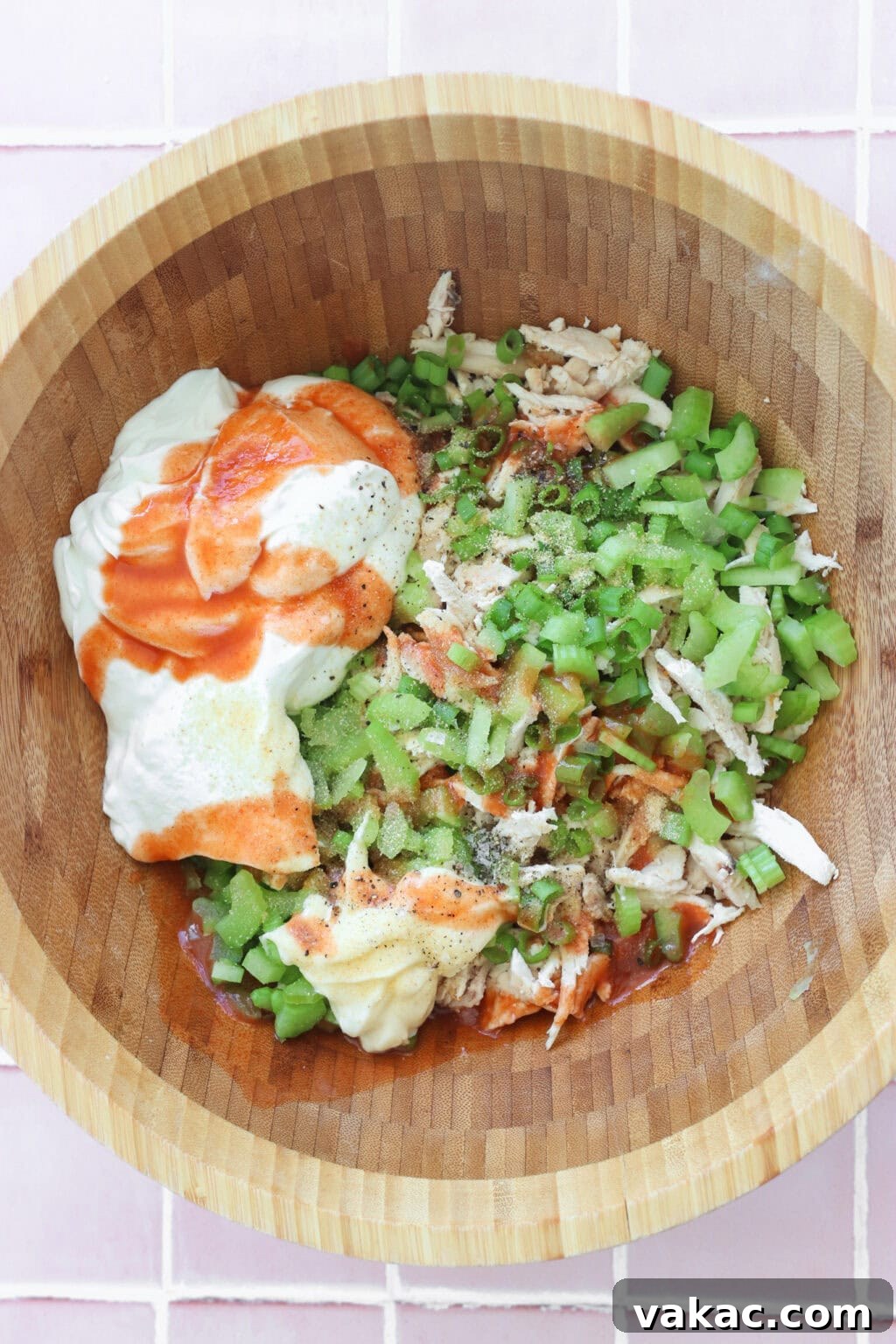 Fast Protein-Packed Buffalo Chicken Salad with Greek Yogurt 4 Ingredients for Quick Buffalo Chicken Salad with Greek Yogurt unmixed in a medium wooden bowl including cooked shredded chicken, Greek yogurt, mayo, Frank's Red Hot Original Sauce, garlic powder, green onions, blue cheese, pepper