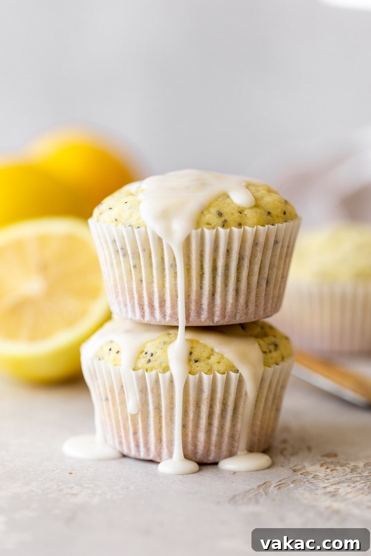 Zesty Lemon Poppy Seed Muffins 6 Two irresistibly moist Lemon Poppy Seed Muffins, stacked one on top of the other, showcasing a generous drizzle of lemon glaze cascading down their sides, inviting you to take a bite.