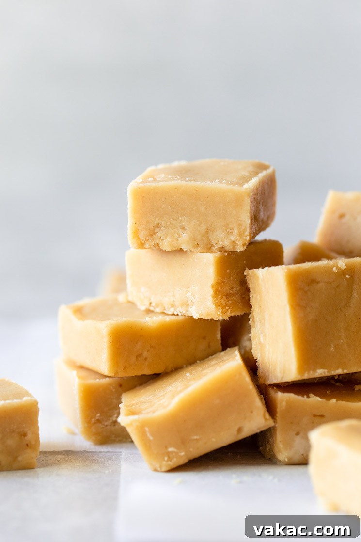 Ultimate Peanut Butter Fudge 2 Pieces of peanut butter fudge stacked on a gray surface lined with parchment paper.
