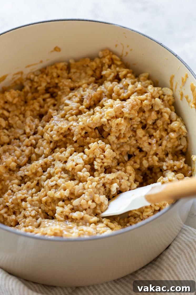 Peanut Butter Butterscotch Crispy Bars 4 A white saucepan showing crispy rice cereal being gently folded into the warm, melted peanut butter, corn syrup, and sugar mixture, ensuring every piece of cereal is evenly coated.