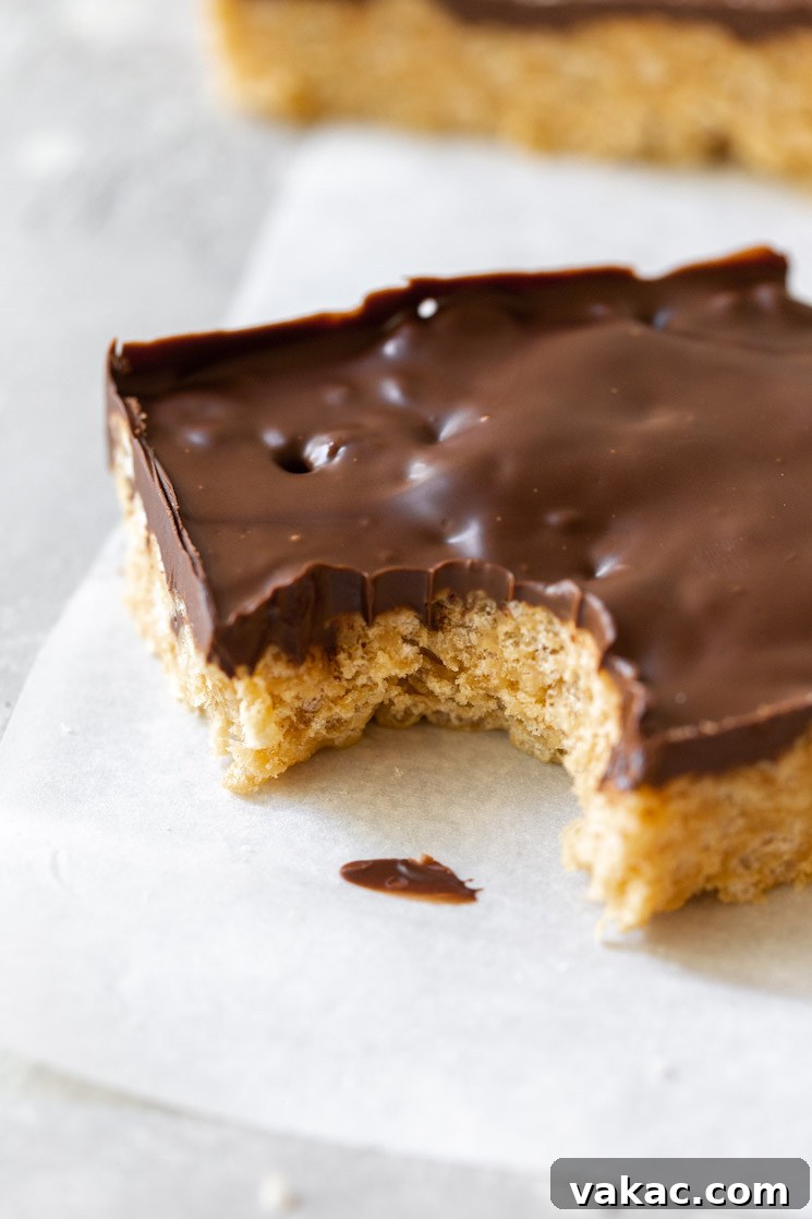 Peanut Butter Butterscotch Crispy Bars 6 A single Scotcheroo bar on a piece of parchment paper, with a bite taken out, clearly displaying the perfectly formed layers of the crunchy peanut butter base and the smooth chocolate butterscotch topping.