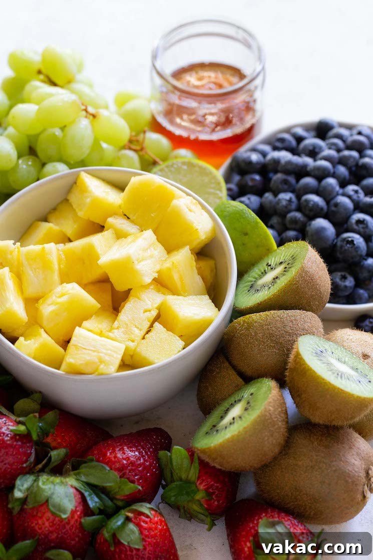 Sun Kissed Fruit Delight 3 A colorful array of fresh fruit ingredients for the fruit salad, including strawberries, pineapple, blueberries, grapes, and kiwis, neatly arranged on a rustic gray surface.