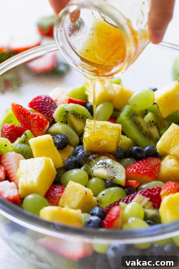 Sun Kissed Fruit Delight 4 A clear glass bowl showcasing a colorful fruit salad as a honey-lime dressing is gracefully poured over it from a separate glass jar, creating a glistening coating.