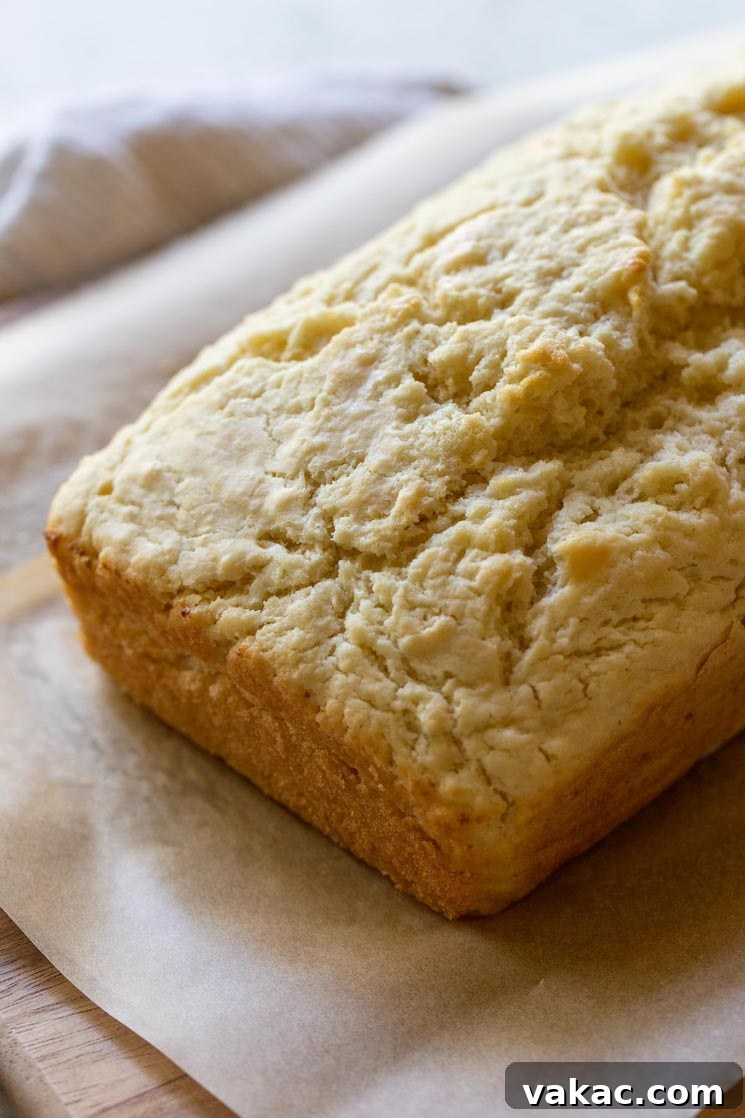 Golden Brew Loaf 2 A golden-brown loaf of beer bread resting on a rustic wood cutting board, emitting steam as it cools, showcasing its inviting texture.