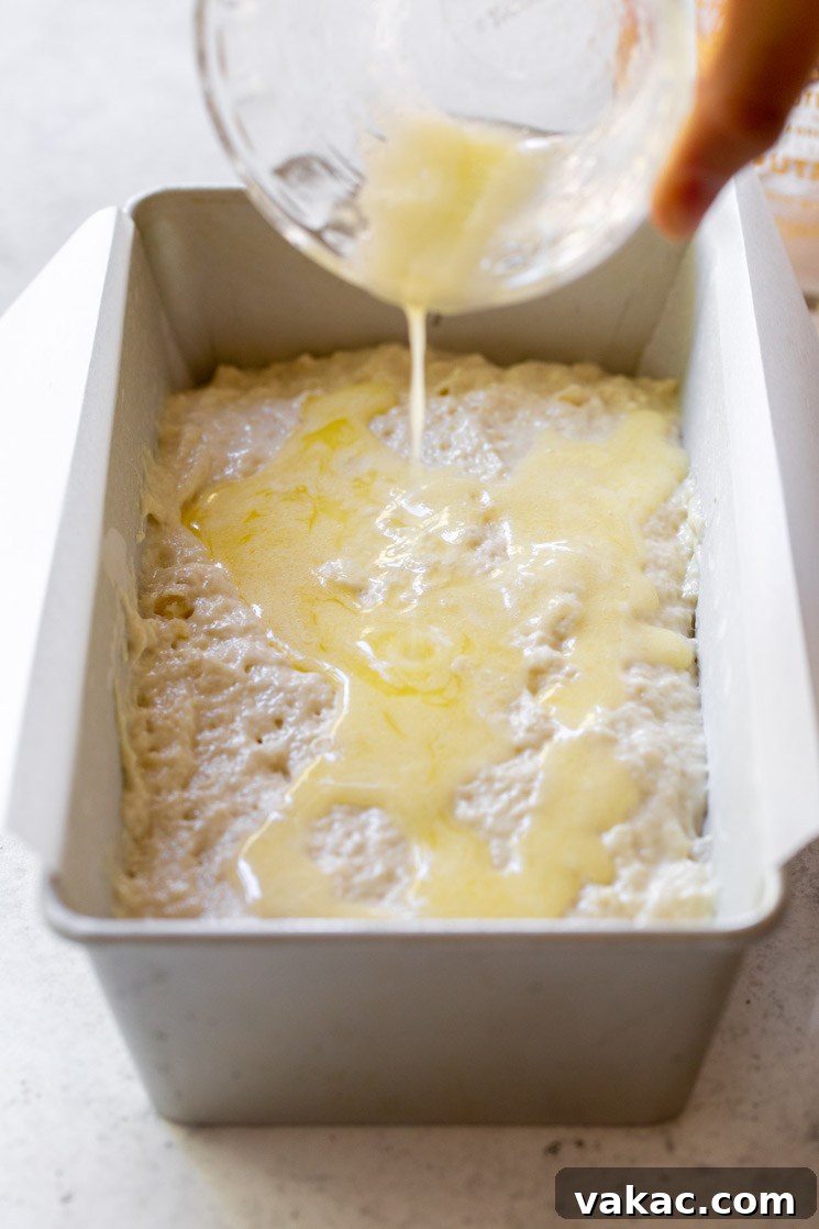 Golden Brew Loaf 5 A metal loaf pan holding the unbaked beer bread batter, with additional melted butter being generously poured over the top of the batter.