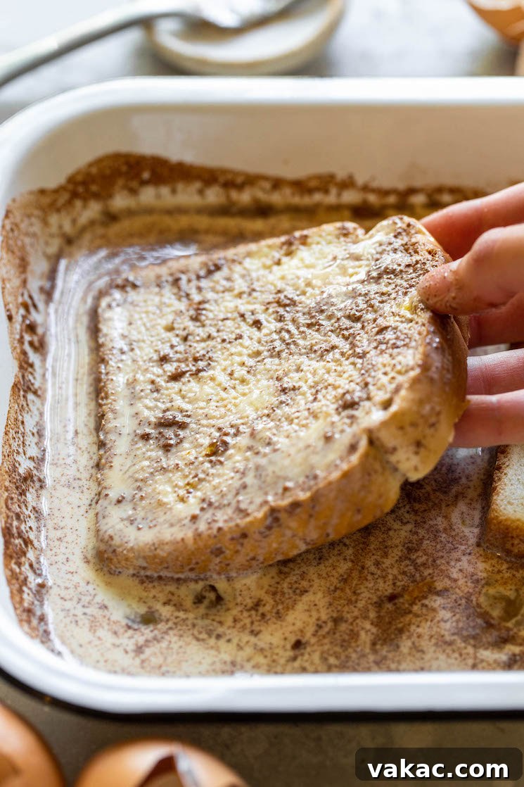 Unforgettable French Toast 5 A slice of bread being carefully dipped into the egg mixture, showing how it should be completely covered and allowed to absorb the custard.