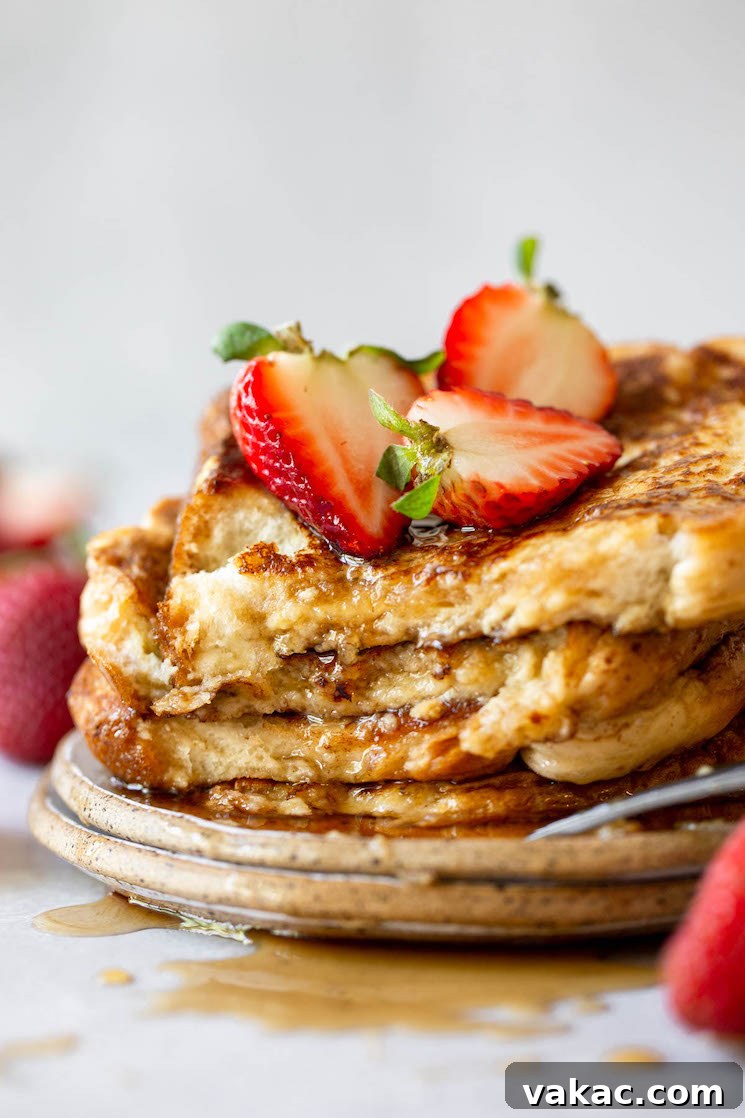 Unforgettable French Toast 7 A plate featuring a stack of golden French toast, generously drizzled with pure maple syrup and garnished with fresh halved strawberries.