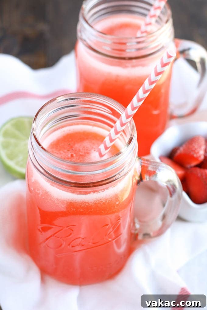 Blushing Berry Zest 2 Fresh Strawberry Limeade served in a clear glass pitcher with sliced strawberries and limes, garnished with mint