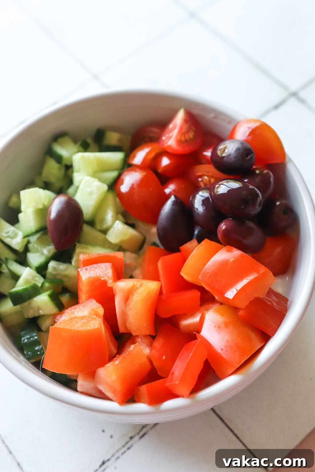 Zesty Mediterranean Cottage Cheese Salad 4 Ingredients for Easy Greek-Inspired Cottage Cheese Salad unmixed in a white bowl, including cherry tomatoes, cucumber, red peppers, and olives.