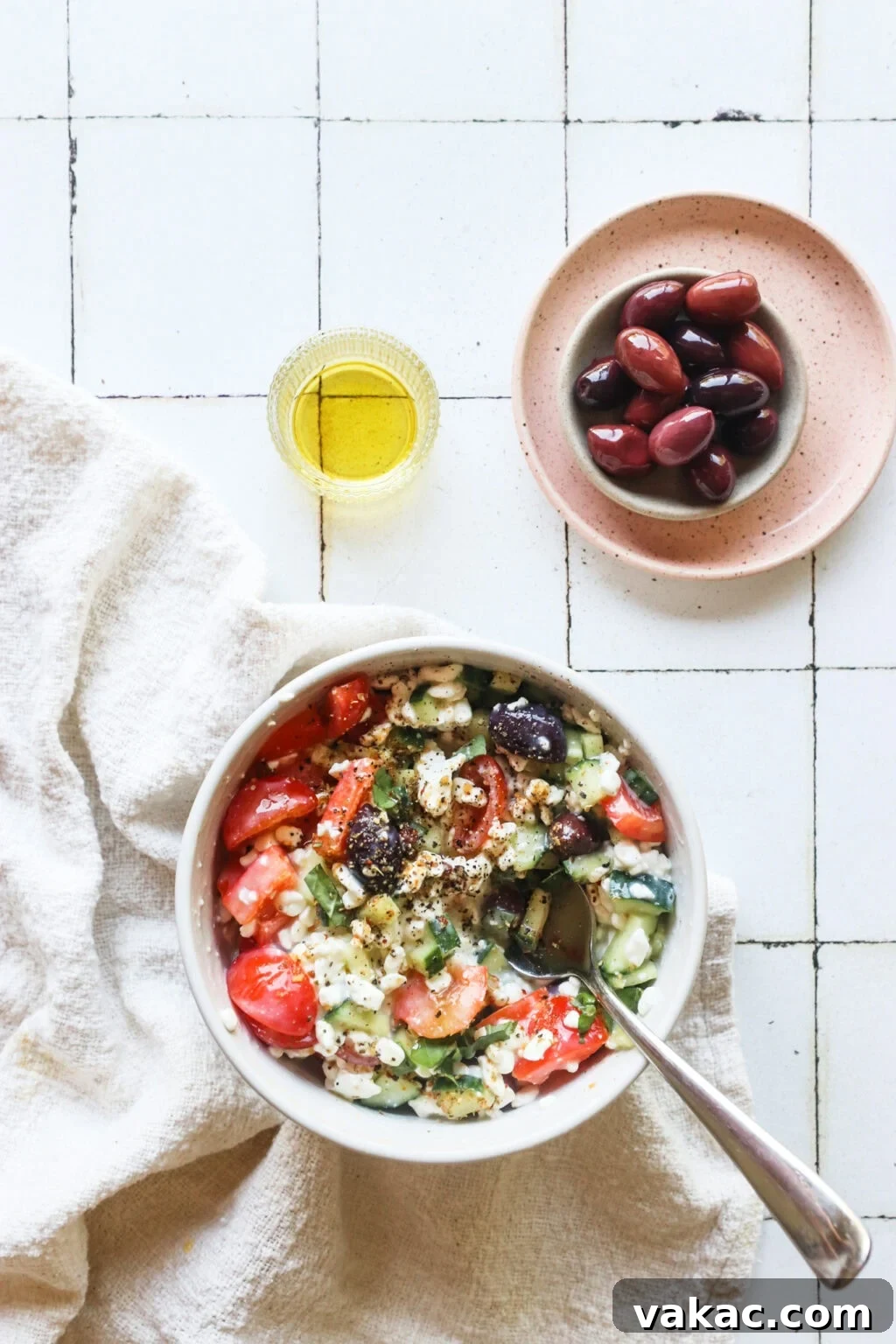 Zesty Mediterranean Cottage Cheese Salad 8 Easy Greek-Inspired Cottage Cheese Salad in a white bowl with a pink plate of olives on the side, ready to be served.
