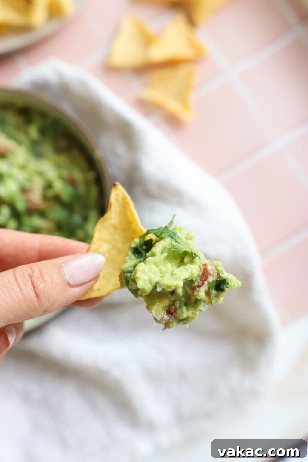 Speedy Creamy Greek Yogurt Guacamole 2 Creamy 5-Minute Guacamole Dip with Greek Yogurt served on a tortilla chip with a white bowl in the background