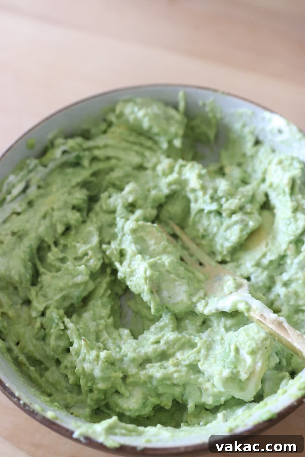 Speedy Creamy Greek Yogurt Guacamole 6 Mashing avocados with a fork in a white bowl to achieve the desired consistency