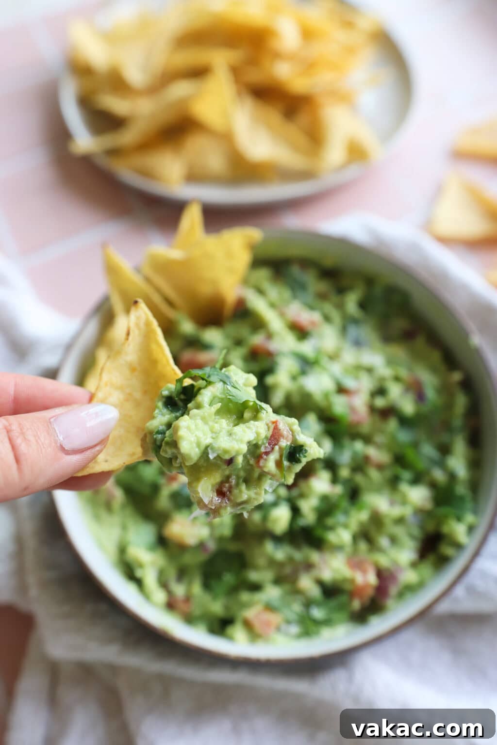 Speedy Creamy Greek Yogurt Guacamole 9 5-Minute Greek Yogurt Guacamole Dip served on a tortilla chip with a white bowl of dip in the background