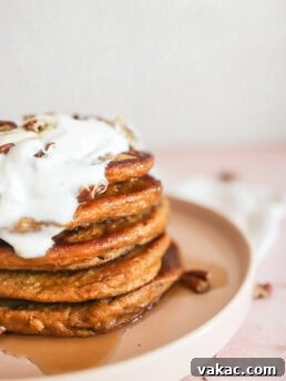 A stack of High Protein Pumpkin Pancakes with Cottage Cheese on a pink plate with a dollop of Greek yogurt