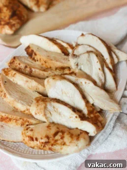 Cooked and sliced seasoned chicken breasts on a white serving dish with a white dish towel on the side