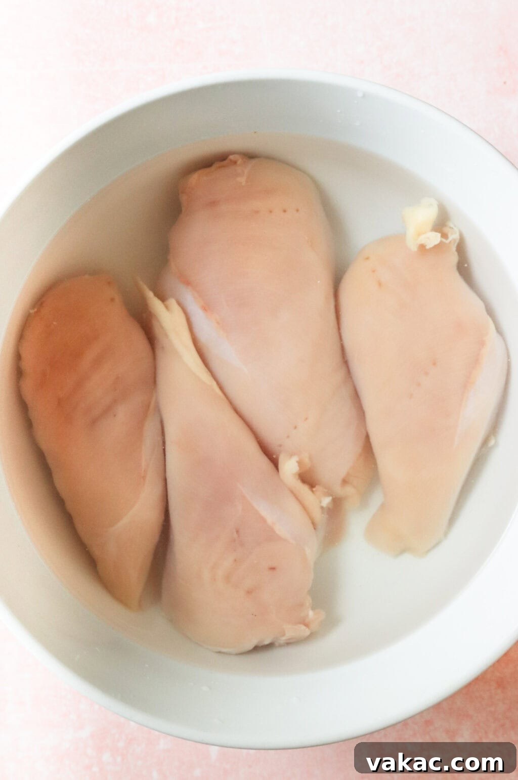 Succulent Oven Baked Thin Chicken Breast 4 Four chicken breasts soaking in salt water in a white bowl.