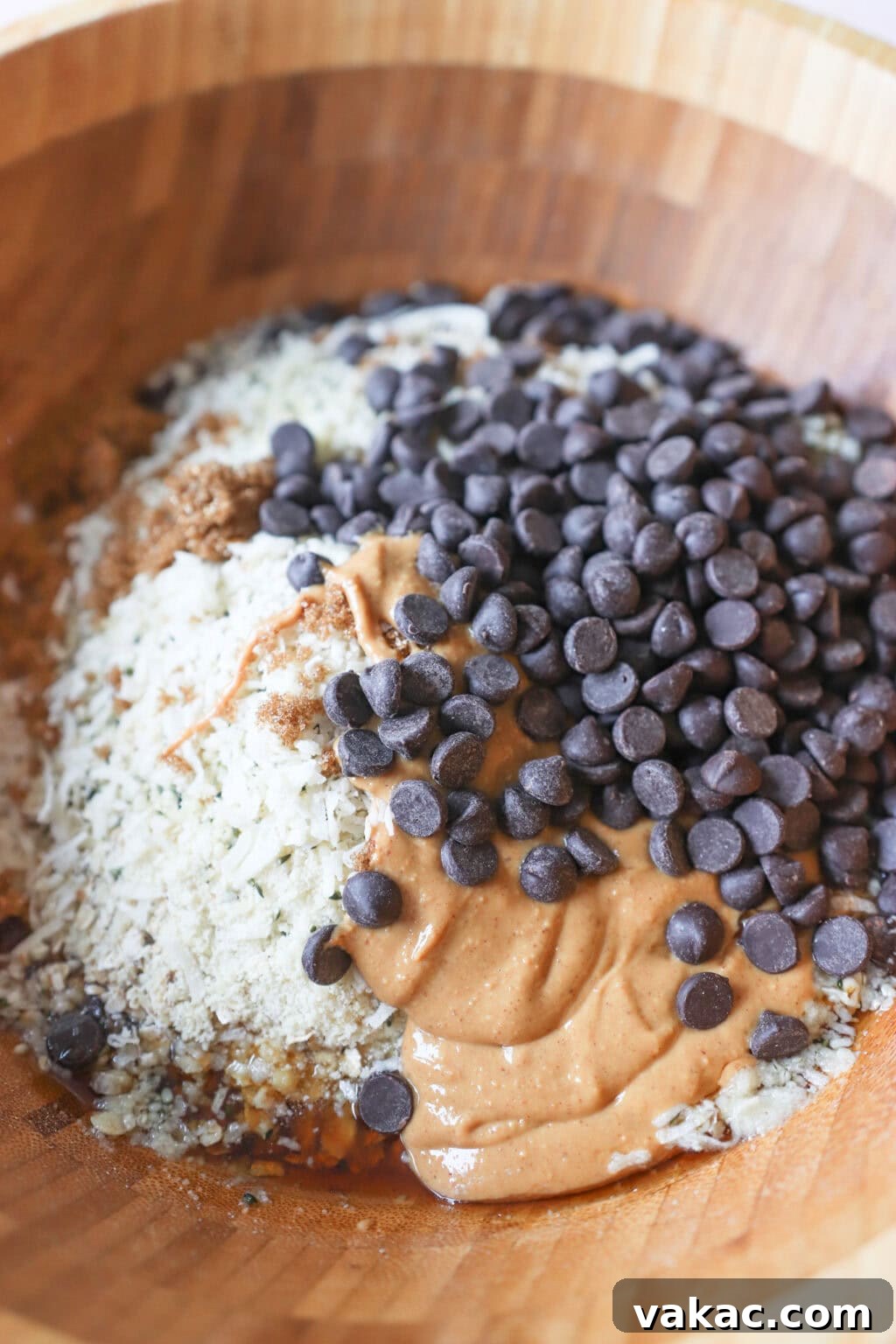 Homemade Heavenly Hunks: So Good, You'll Never Buy Them Again 4 All ingredients for Homemade Heavenly Hunks unmixed in a large mixing bowl, showing rolled oats, almond flour, coconut flakes, hemp hearts, maple syrup, coconut oil, peanut butter, brown sugar, salt, and chocolate chips