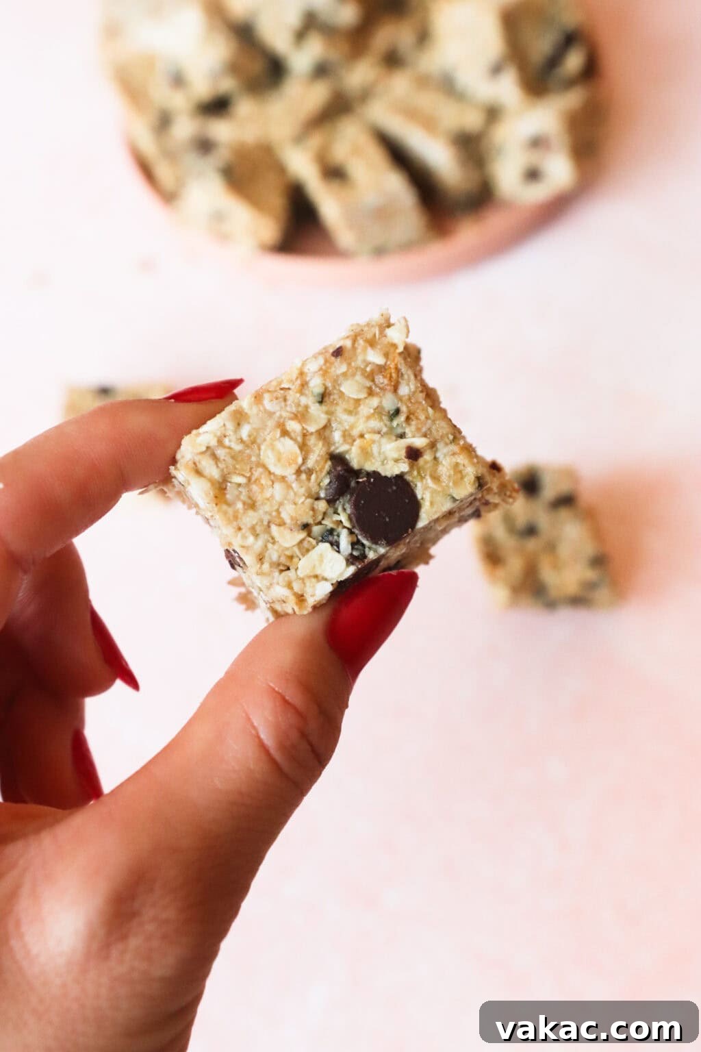 Homemade Heavenly Hunks: So Good, You'll Never Buy Them Again 8 A hand holding one perfectly sliced Homemade Heavenly Hunk, showcasing its chewy texture and chocolate chips, with a pink plate in the soft background