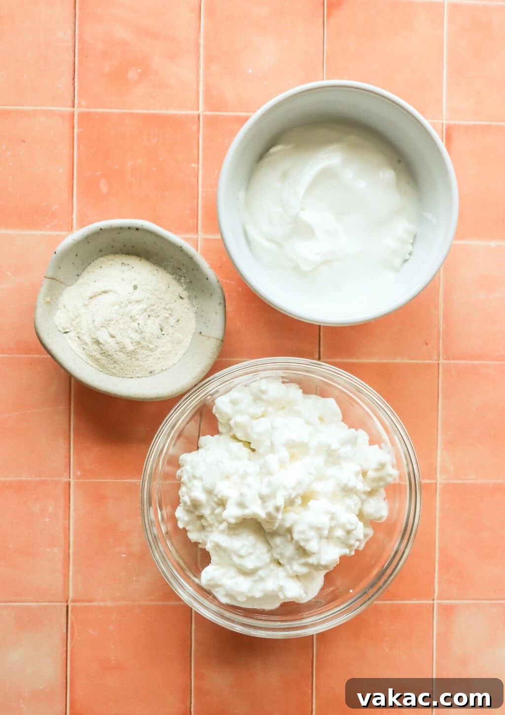 Quick 3-Ingredient Protein Packed Cottage Cheese Ranch Dip 3 Ingredients to make high protein cottage cheese ranch dip in three separate bowls on a orange countertop, glass bowl with cottage cheese, white bowl with greek yogurt and small bowl with ranch seasoning