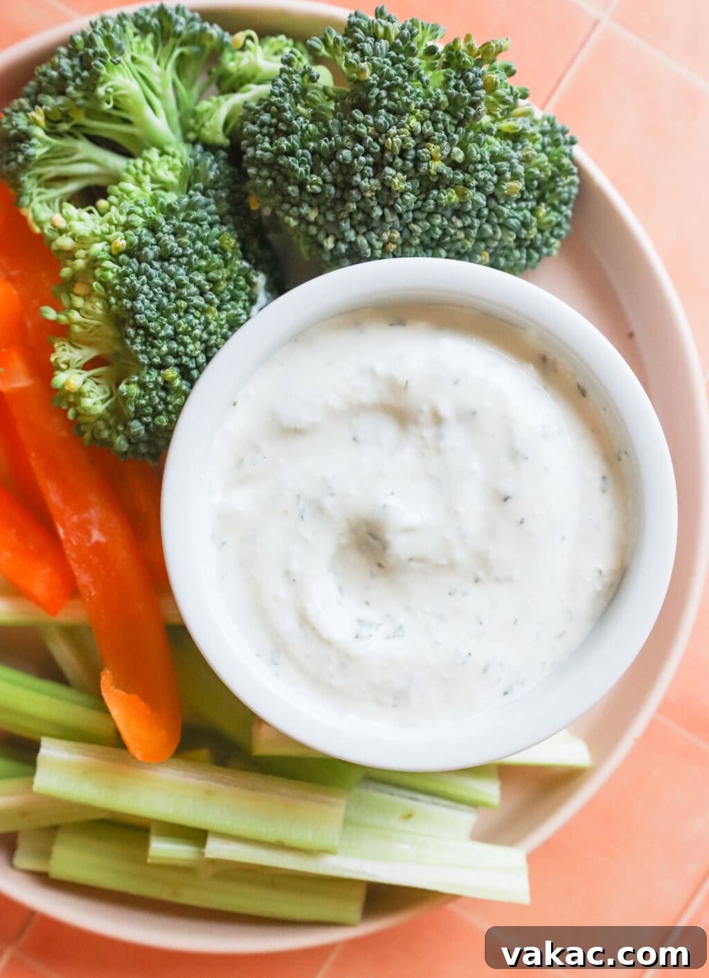 Quick 3-Ingredient Protein Packed Cottage Cheese Ranch Dip 7 final product of the cottage cheese high protein ranch dip, along with celery, red peppers and broccoli on a white plate on an orange counter top