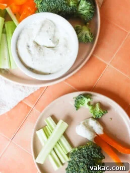 final image of the high protein cottage cheese ranch dip, with celery, peppers and broccoli on a light pink plate, on an orange countertop, and a smaller plate with a few celery sticks, broccoli and peppers dipped in the dip