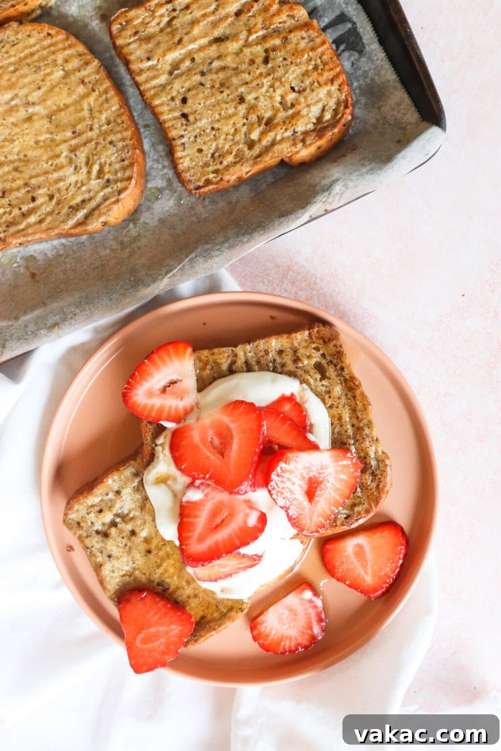 Pillowy Cinnamon-Kissed Sheet Pan French Toast Bake 9 Final product of sheet pan French toast with whipped Greek yogurt and strawberries on top, served on a pink plate with other slices in the background.