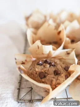 Cottage cheese muffins in brown parchment paper cups rest on a cooling rack, with a soft focus on the background muffins and a crisp view of the muffin in the foreground.