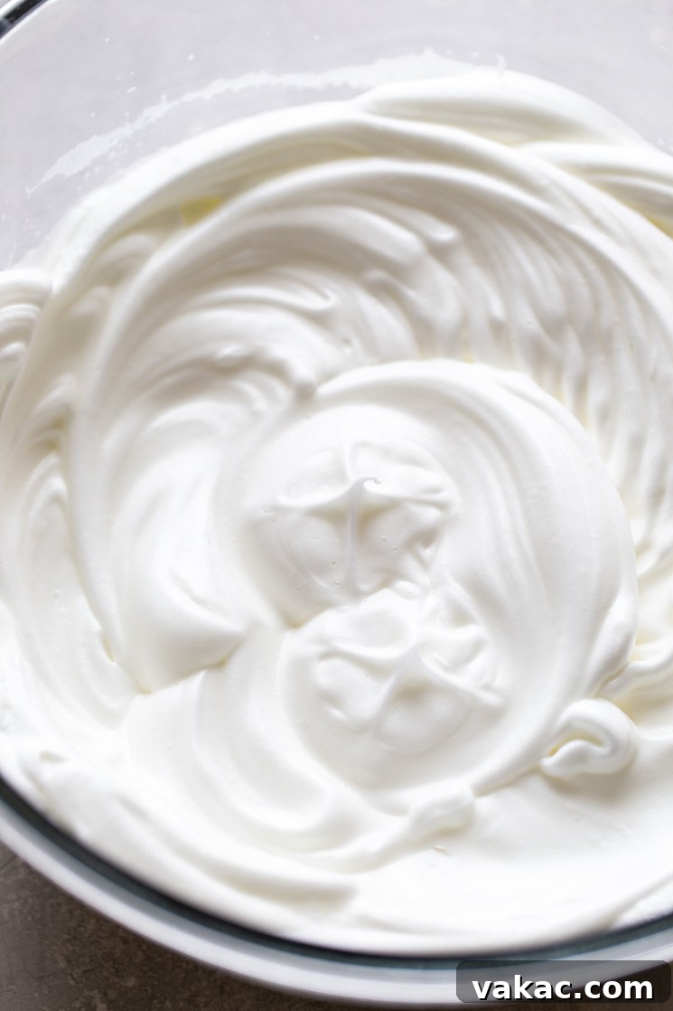 An overhead shot of perfectly whipped egg whites forming stiff peaks in a mixing bowl, ready to be folded into the cake batter.