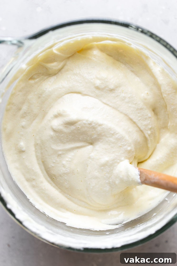 A glass bowl containing fluffy tres leches cake batter, with a spatula gently folding the ingredients, illustrating the delicate mixing process.