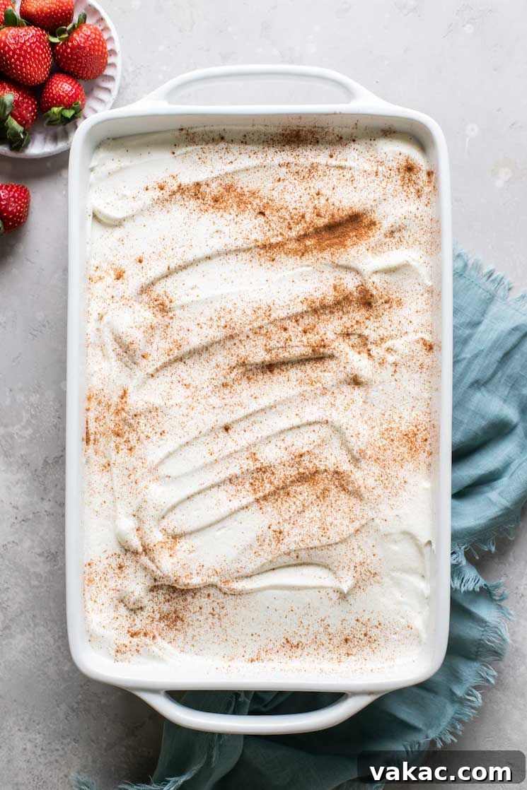 An inviting overhead view of an authentic tres leches cake in a white baking dish, elegantly garnished and ready to serve, with a bowl of vibrant fresh strawberries nearby.