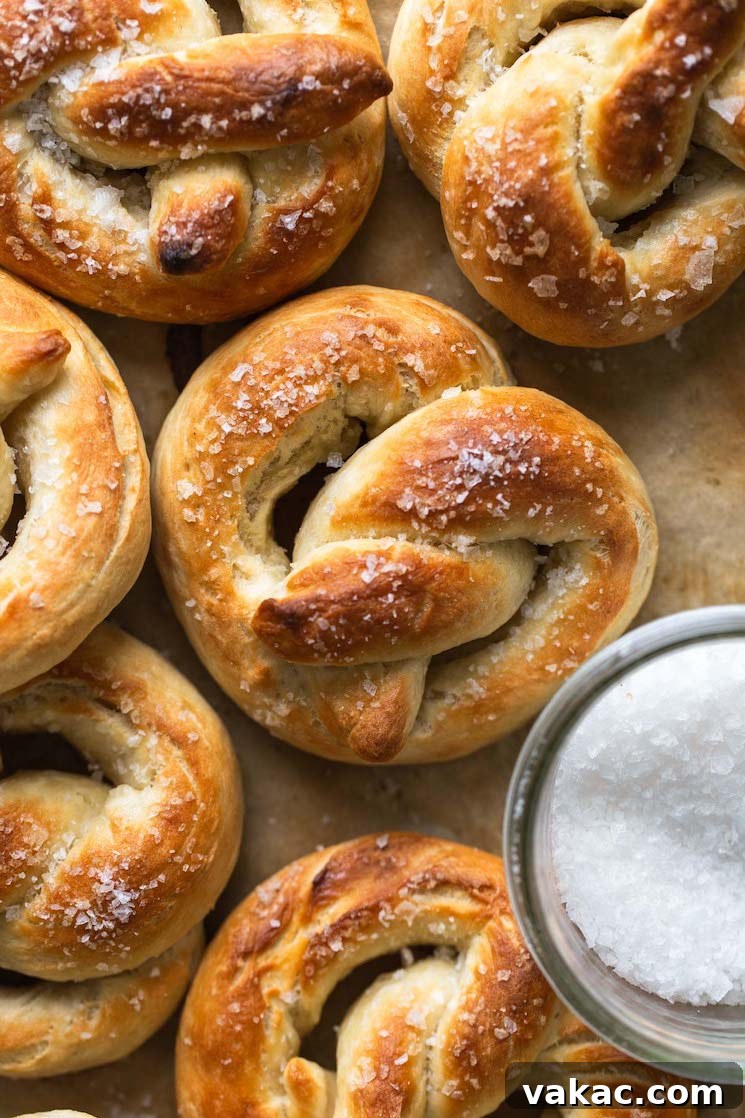Bakery-Style Soft Pretzels 2 Overhead view of perfectly golden-brown homemade soft pretzels on parchment paper, ready to be served. A small dish of coarse salt sits beside them.