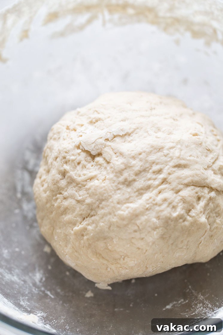 A perfectly formed ball of soft pretzel dough in a glass mixing bowl, ready for its brief rest.