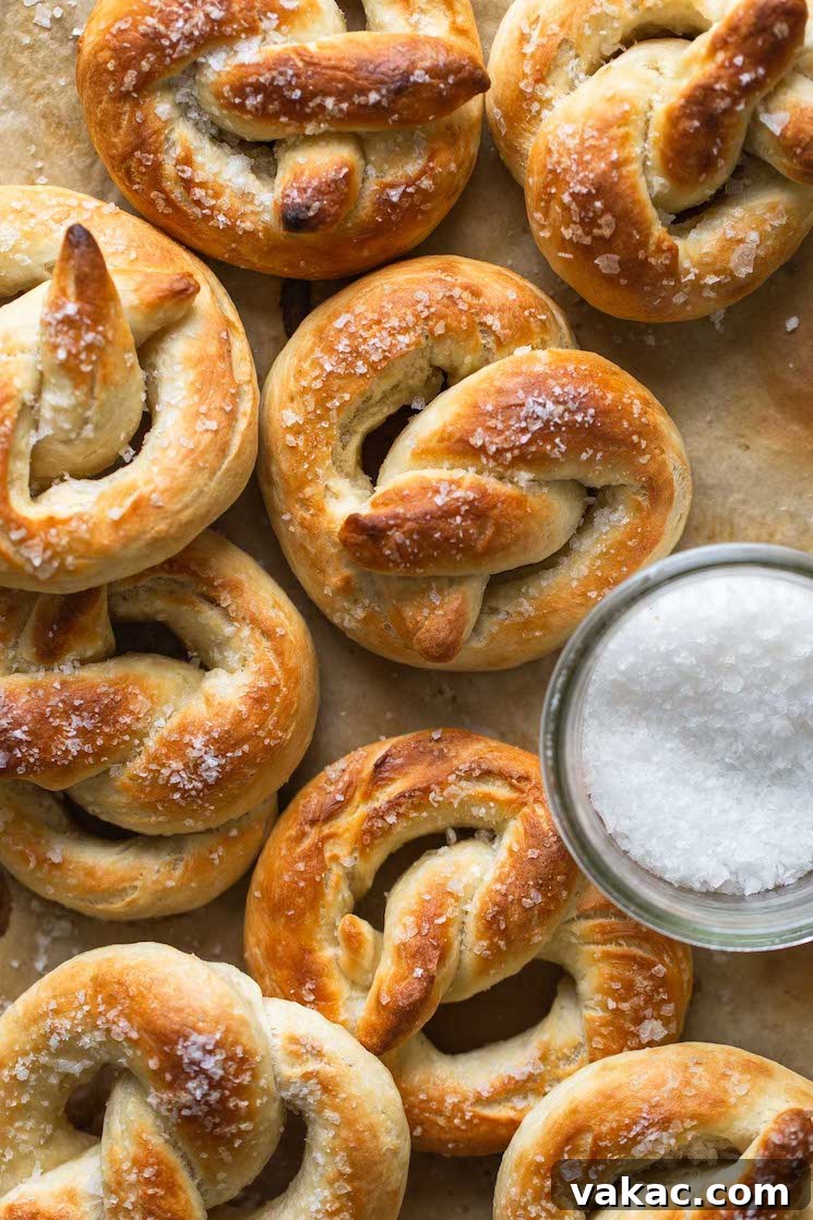 Bakery-Style Soft Pretzels 8 Overhead view of several freshly baked soft pretzels arranged next to a small dish filled with coarse salt, showcasing their perfect golden-brown crust.