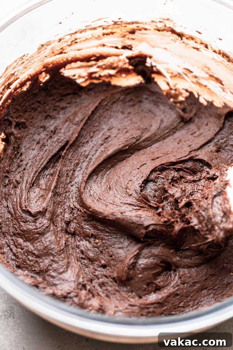 A glass mixing bowl holds the rich, dark chocolate cookie dough, which has a consistency similar to brownie batter, ready to be chilled.