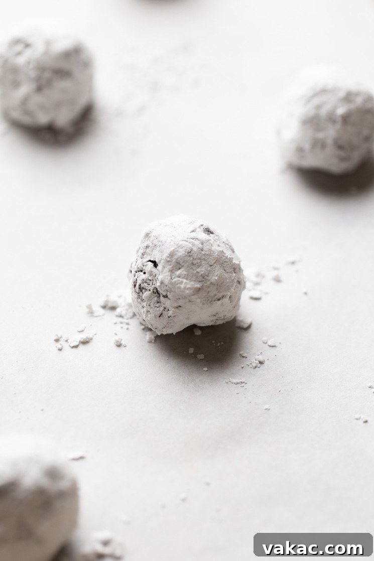 A baking sheet lined with parchment paper, holding several uniformly sized balls of chocolate cookie dough, each generously coated in powdered sugar and spaced for even baking.