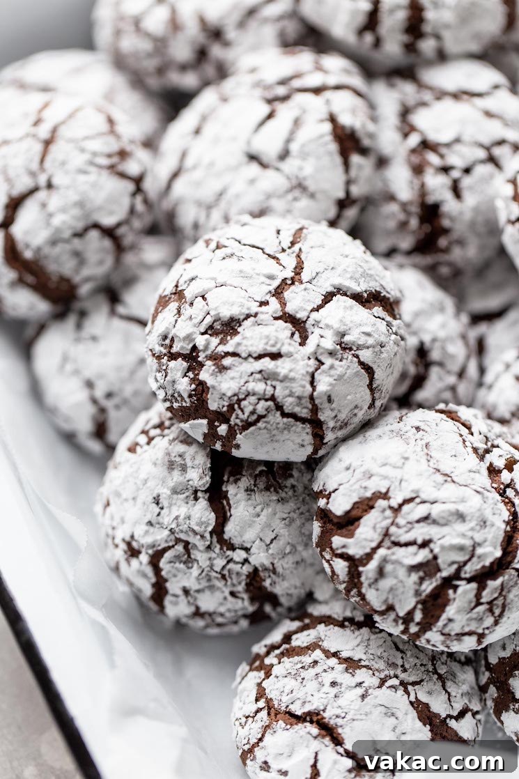 A festive white serving dish brimming with a generous pile of chocolate crinkle cookies, their dark centers peeking through snowy powdered sugar, ready for sharing.