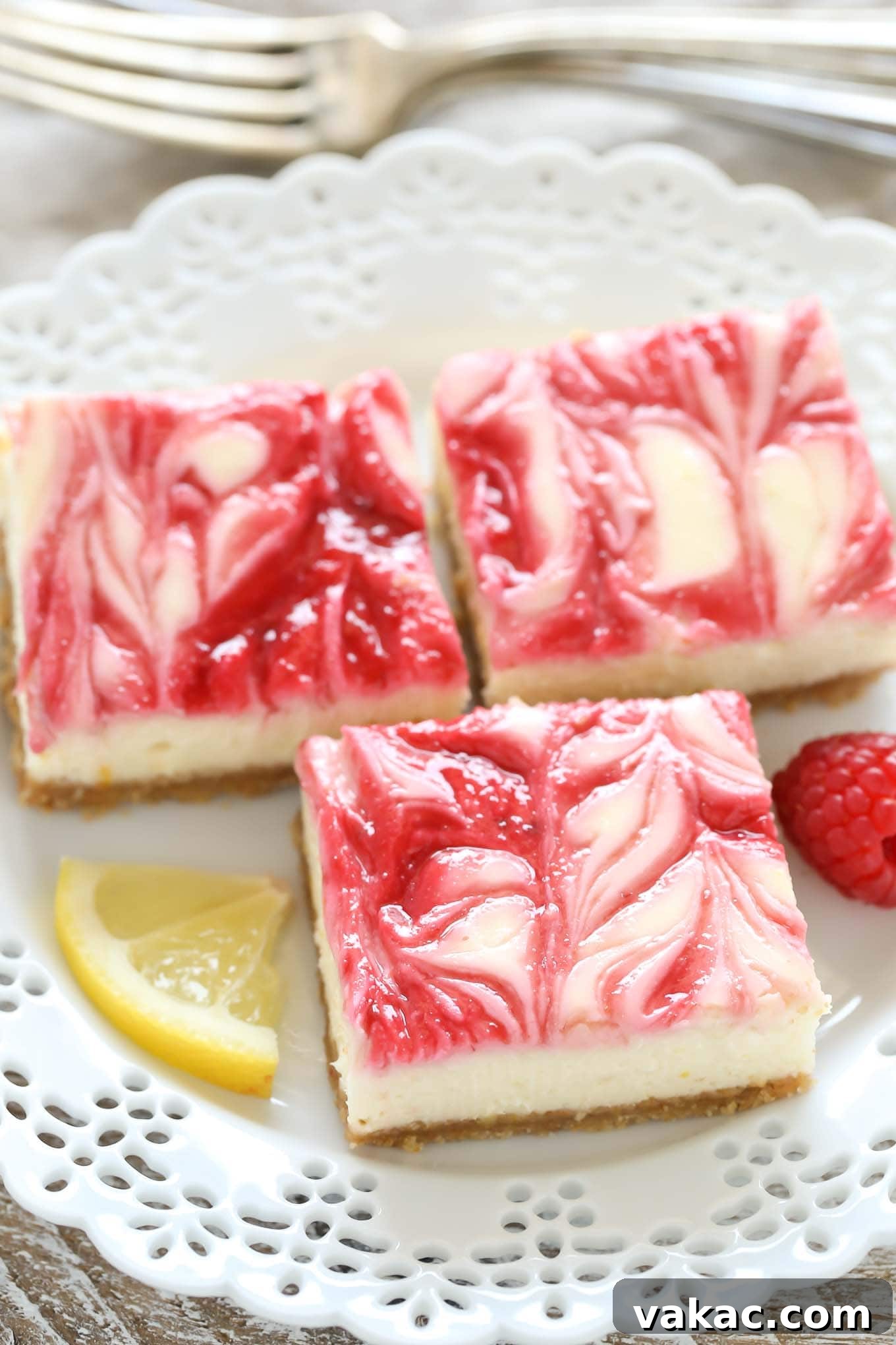 Zesty Lemon Raspberry Cheesecake Bars 2 Three lemon raspberry cheesecake bars arranged elegantly on a pristine white dessert plate, showcasing their vibrant colors and creamy texture.