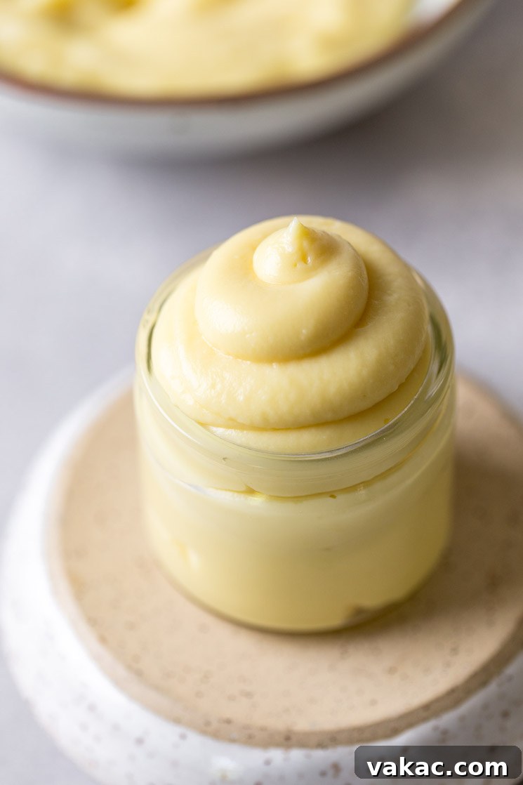 A small glass jar filled with vanilla pastry cream. The jar rests on an overturned bowl. More pastry cream rests in the background.