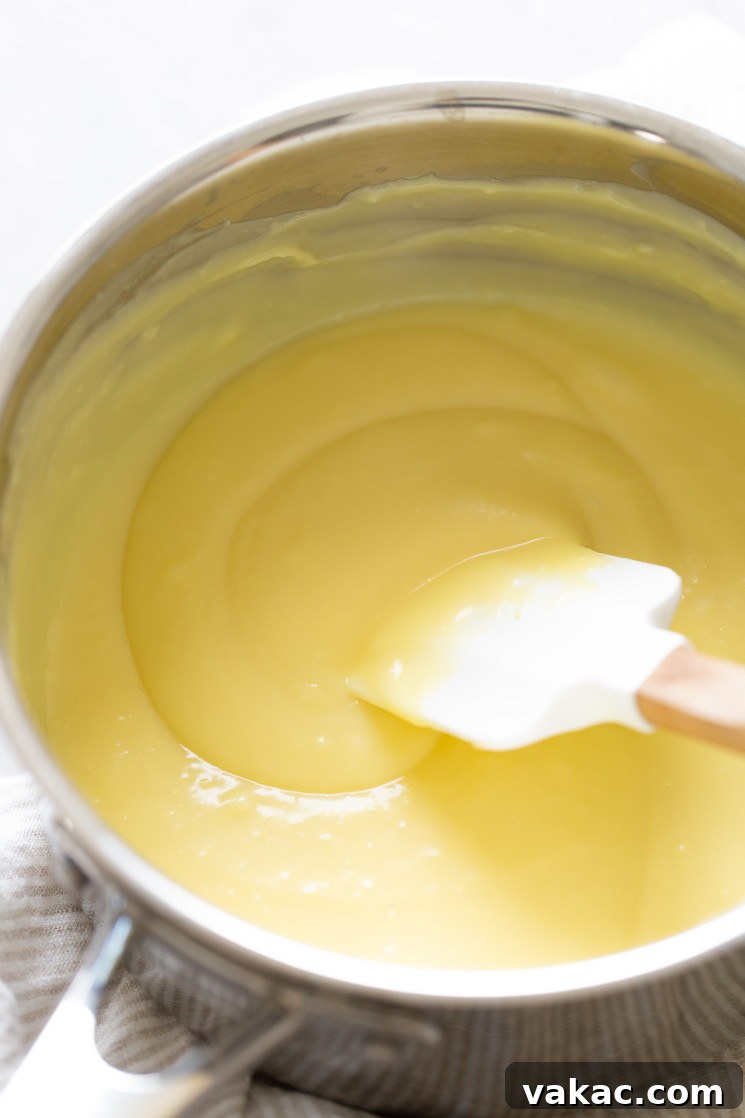 Warm pastry cream in a saucepan. A rubber spatula rests inside the pan.