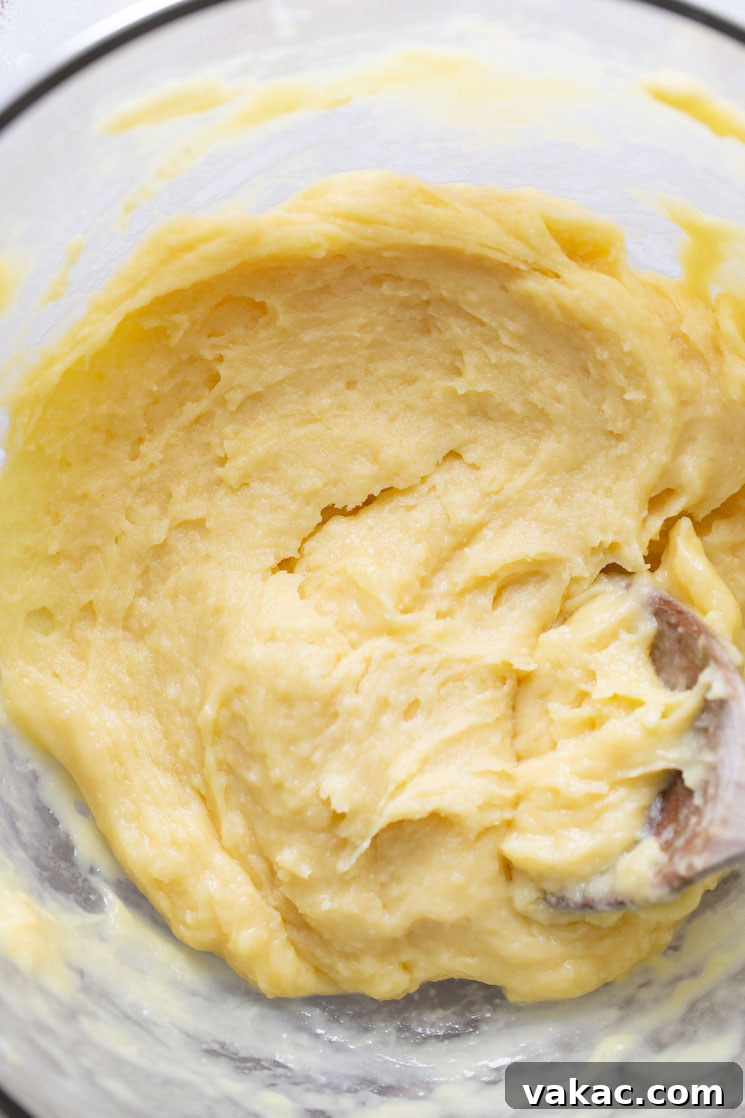 Choux pastry dough in a large glass bowl with a wooden spoon.