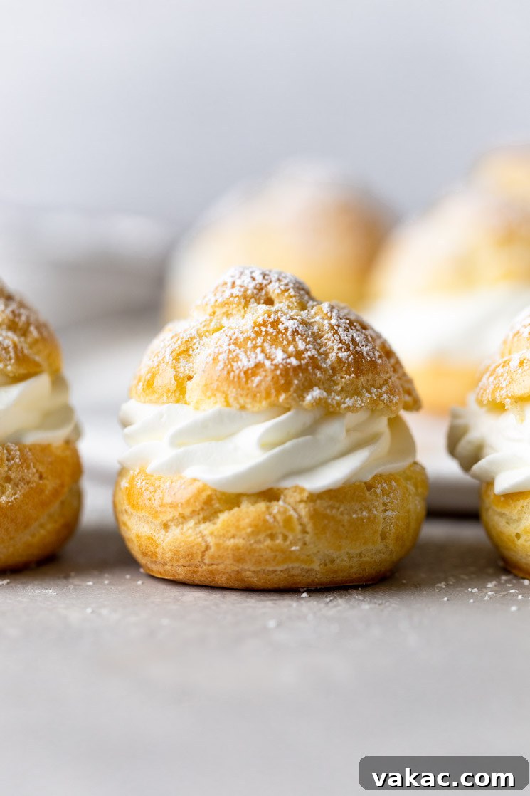 Sweet Cream Clouds 9 Side view of filled cream puffs lined up on a countertop. More cream puffs rest on a plate in the background.