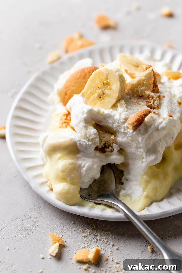 Southern Banana Dream 8 A serving of homemade banana pudding on a white dessert plate. A fork rests on the plate and crushed Nilla Wafers surround it.