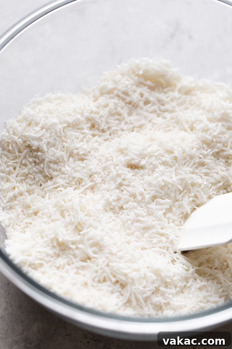 Sweetened shredded coconut in a glass mixing bowl with a rubber spatula.