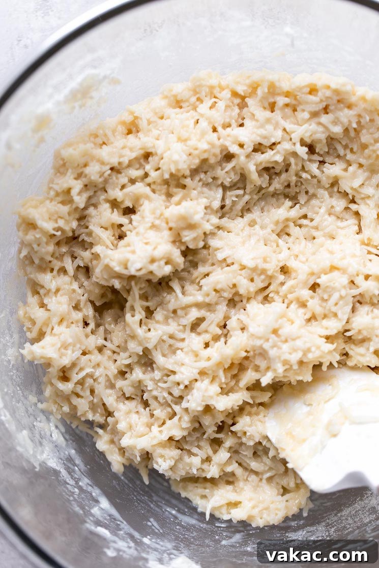 Coconut macaroon dough in a glass mixing bowl with a rubber spatula.