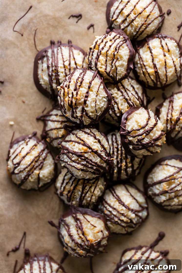 Chewy Toasted Coconut Macaroons 9 A pile of macaroon cookies drizzled with chocolate on parchment paper.