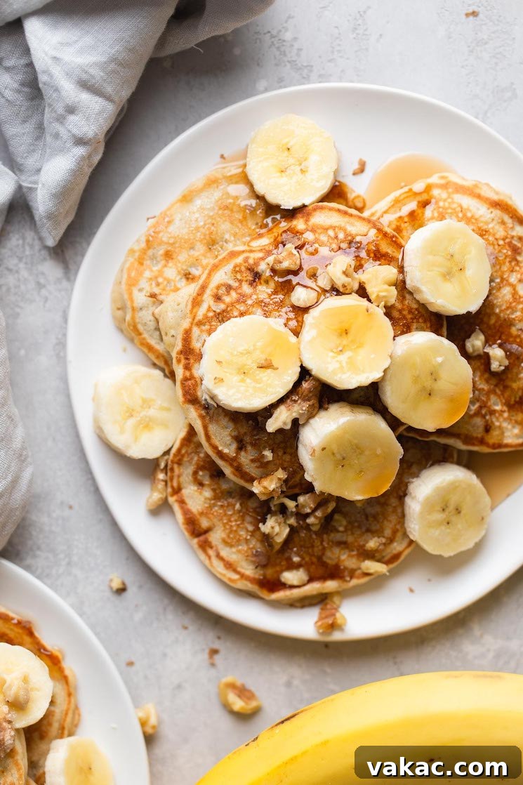 Overhead view of fluffy banana pancakes topped with banana slices and chopped walnuts on a white plate.