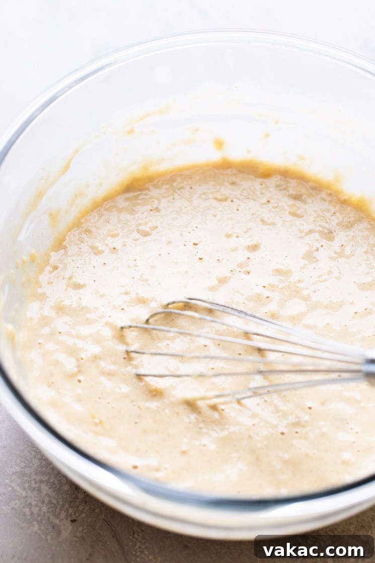 Homemade banana pancake batter with a whisk in a glass mixing bowl.