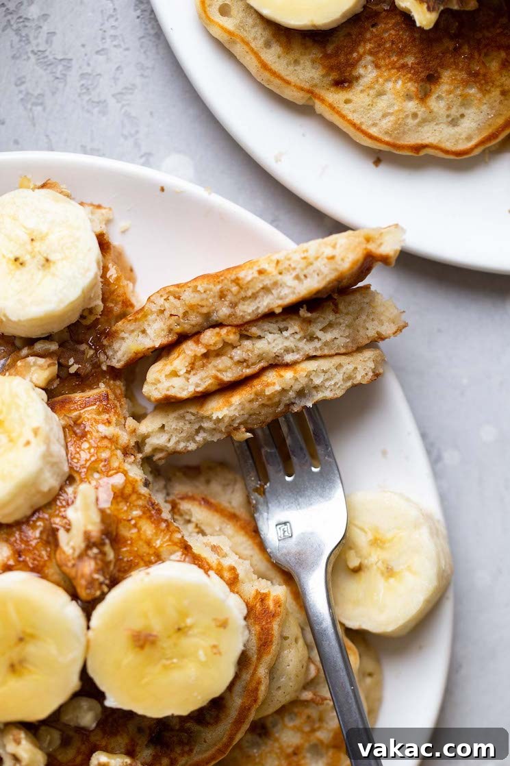 Overhead view of fluffy banana pancakes on a white plate. A fork has speared a bite of pancake.