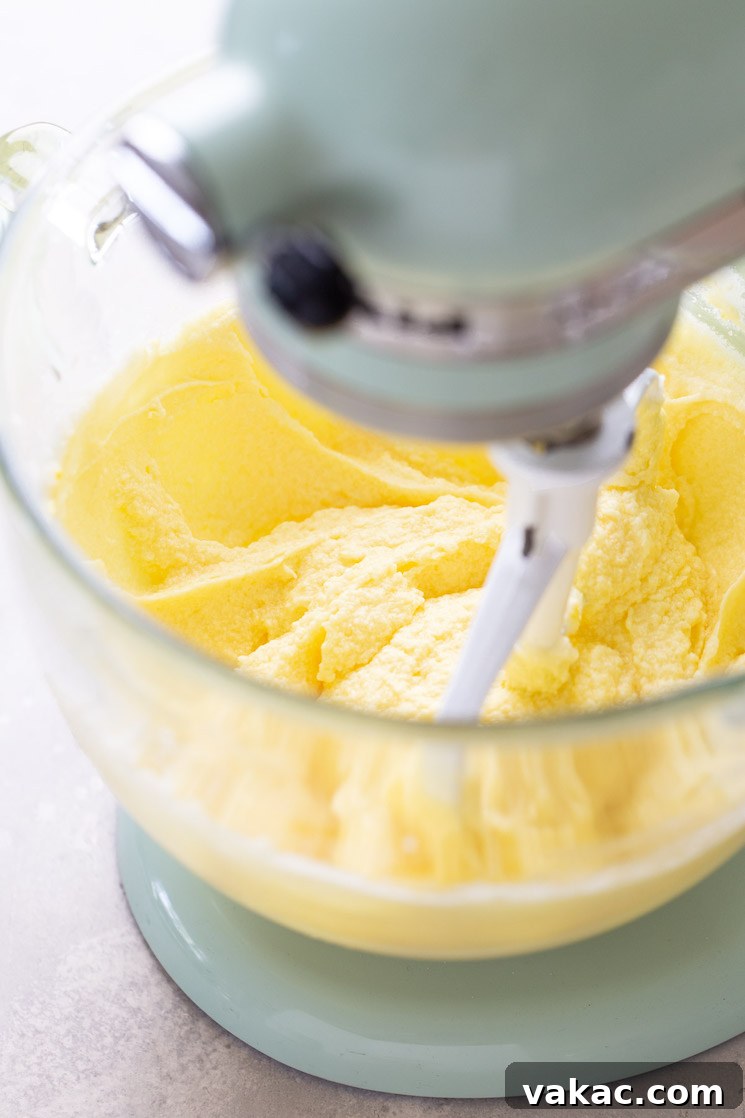 Another process shot demonstrating the precise moment when large eggs are being gradually incorporated into the light and fluffy creamed butter and sugar mixture in a stand mixer, ensuring thorough blending.