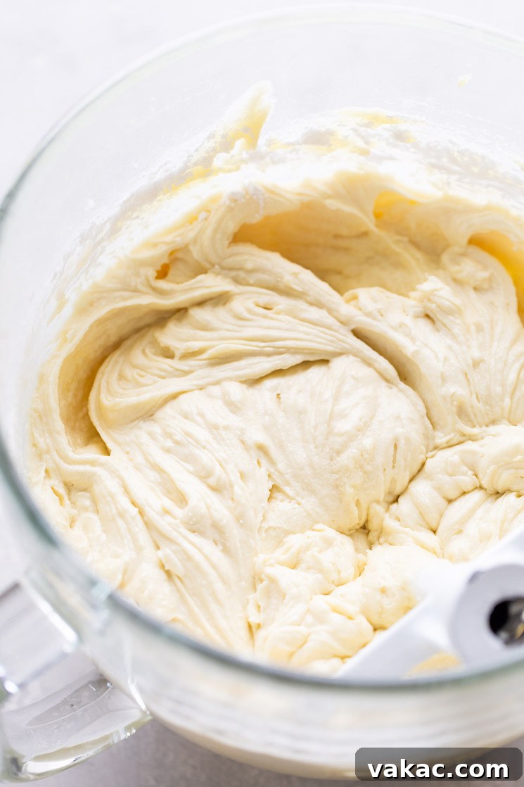 Smooth, pale yellow vanilla cake batter resting gently in a clear glass mixing bowl, with the paddle attachment of a stand mixer visibly immersed in the batter, signaling readiness for baking.